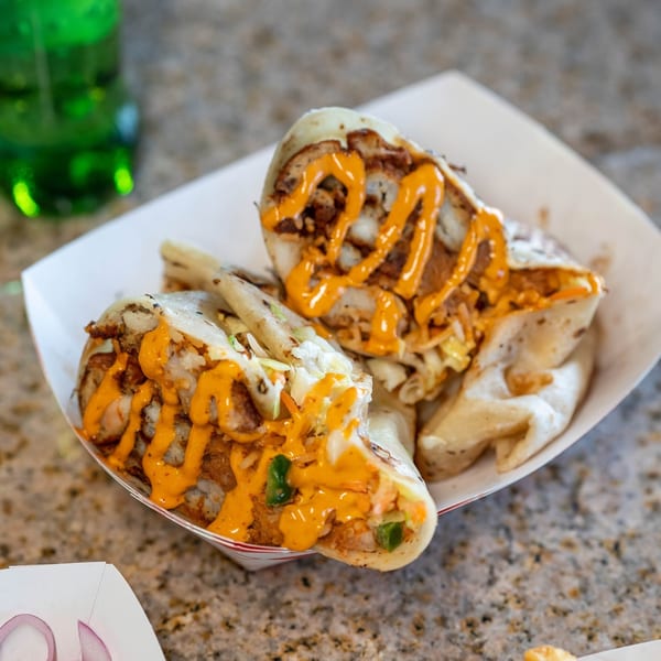 Two Santa Madre Taco Shop burritos, cut in half, drizzled with orange sauce in a paper tray.