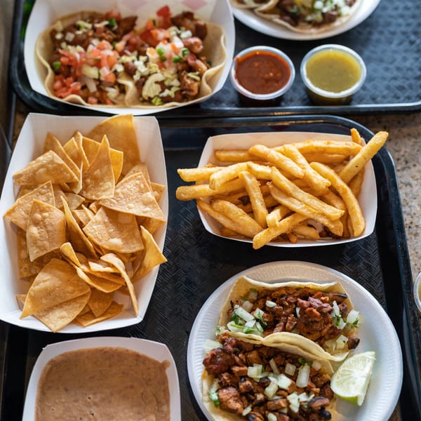 A black tray filled with various Mexican dishes, including tacos, chips, fries, and salsas.
